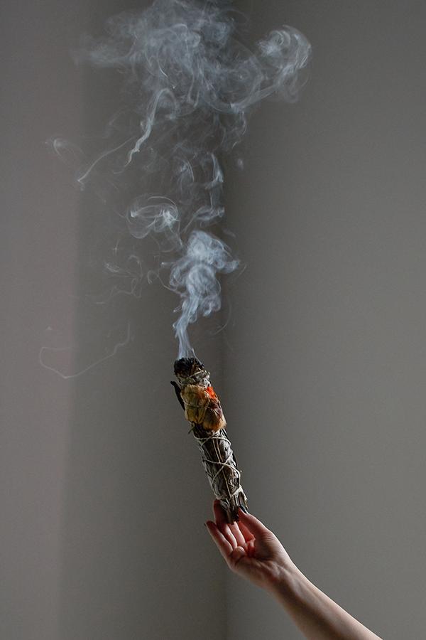 A hand holding burning sage with smoke rising above it
